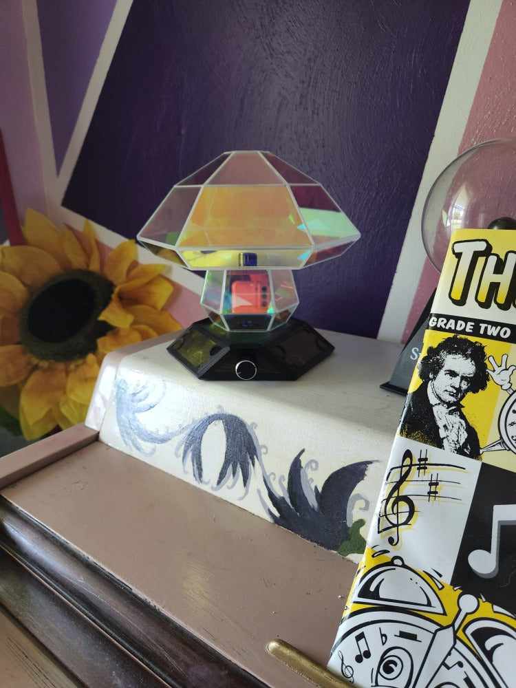 Boletus Lumos lamp, shown on a white piano with a yellow faux sunflower in the background, and purple walls in the room.